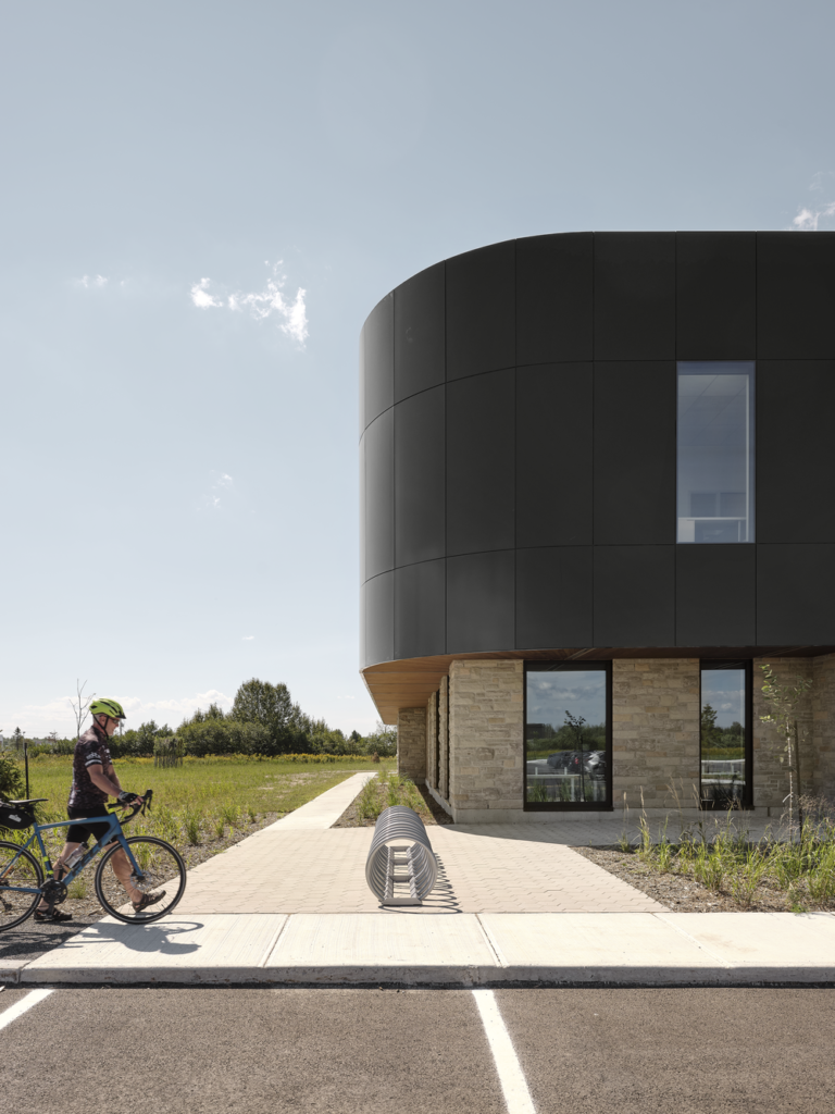 Détail d’un angle courbe de l’Incubateur Bromont : façade noire en panneaux Multifaçades au-dessus d’un socle en pierre.