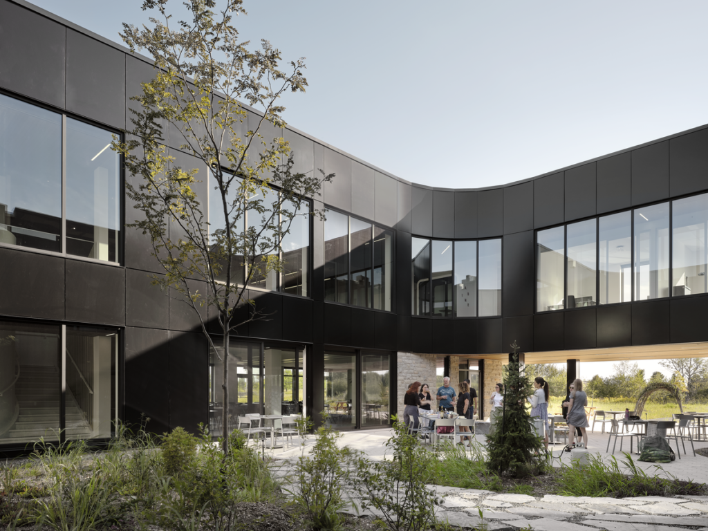 Cour intérieure de l’Incubateur Bromont : façades en panneaux Multifaçades noirs, grandes fenêtres et aménagement paysager central.