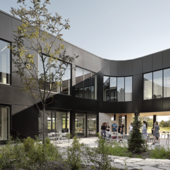 Cour intérieure de l’Incubateur Bromont : façades en panneaux Multifaçades noirs, grandes fenêtres et aménagement paysager central.