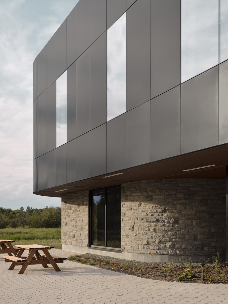 Gros plan de la façade de l’Incubateur Bromont : panneaux d’aluminium Multifaçades, fenêtre verticale et base en pierre.