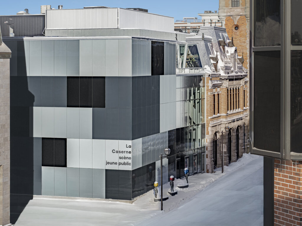 Extension contemporaine en verre opaque et mur-rideau du Théâtre des Gros Becs à Québec, adjacente à une façade patrimoniale en brique et pierre.