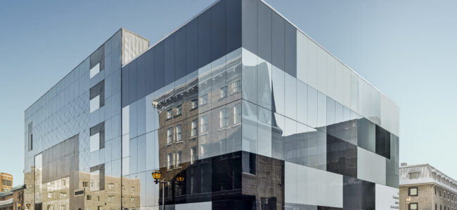 Détail de la façade en verre opaque du Théâtre des Gros Becs à Québec : panneaux gris et noirs en damier, avec volume vitré adjacent.