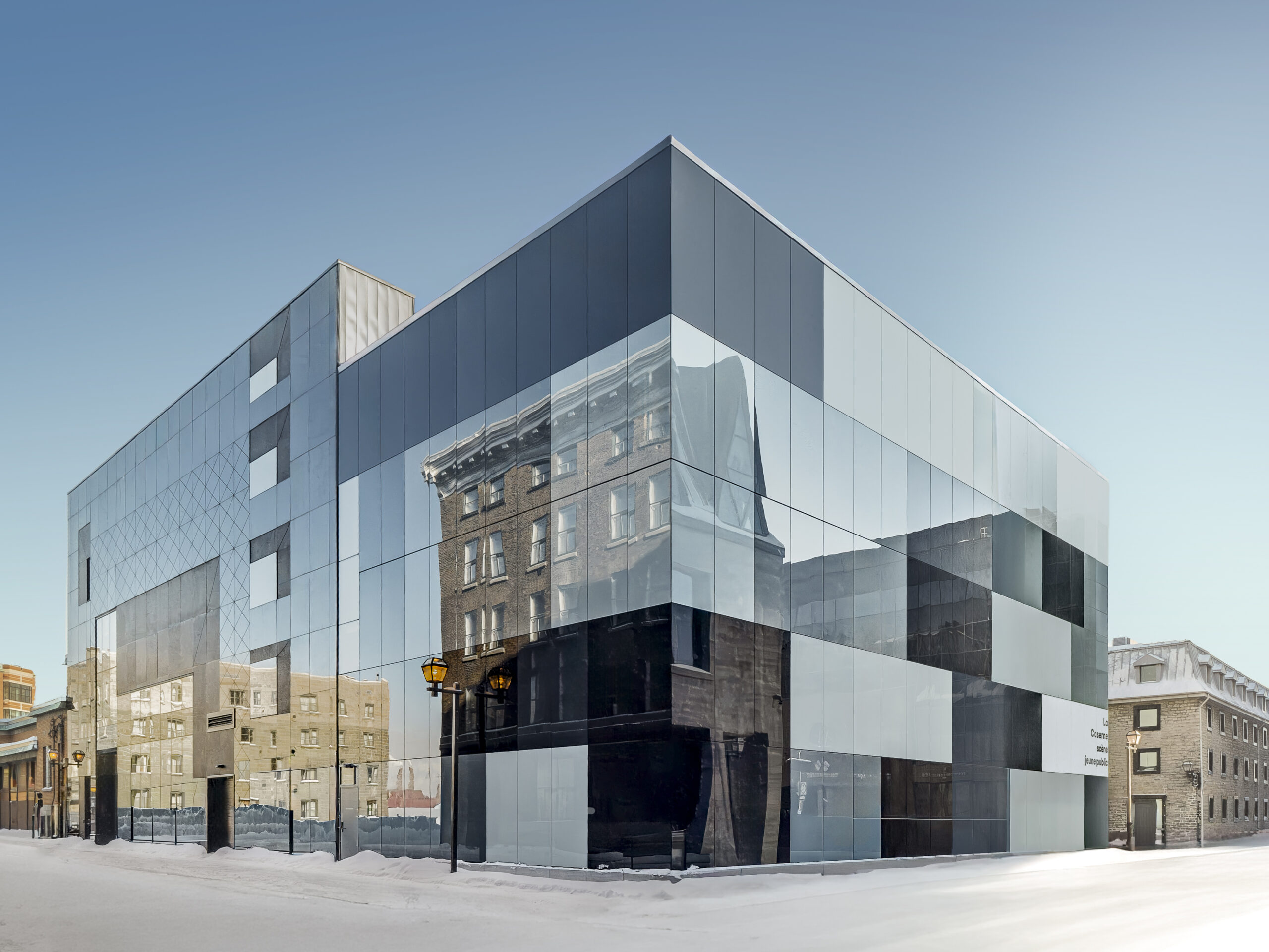Détail de la façade en verre opaque du Théâtre des Gros Becs à Québec : panneaux gris et noirs en damier, avec volume vitré adjacent.