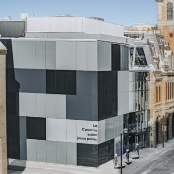 Vue d’ensemble du Théâtre des Gros Becs à Québec : extension moderne vitrée attenante à un bâtiment patrimonial en maçonnerie, en hiver.
