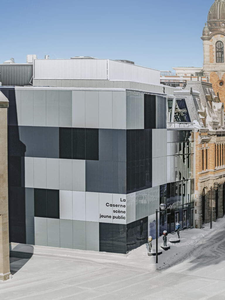 Vue d’ensemble du Théâtre des Gros Becs à Québec : extension moderne vitrée attenante à un bâtiment patrimonial en maçonnerie, en hiver.